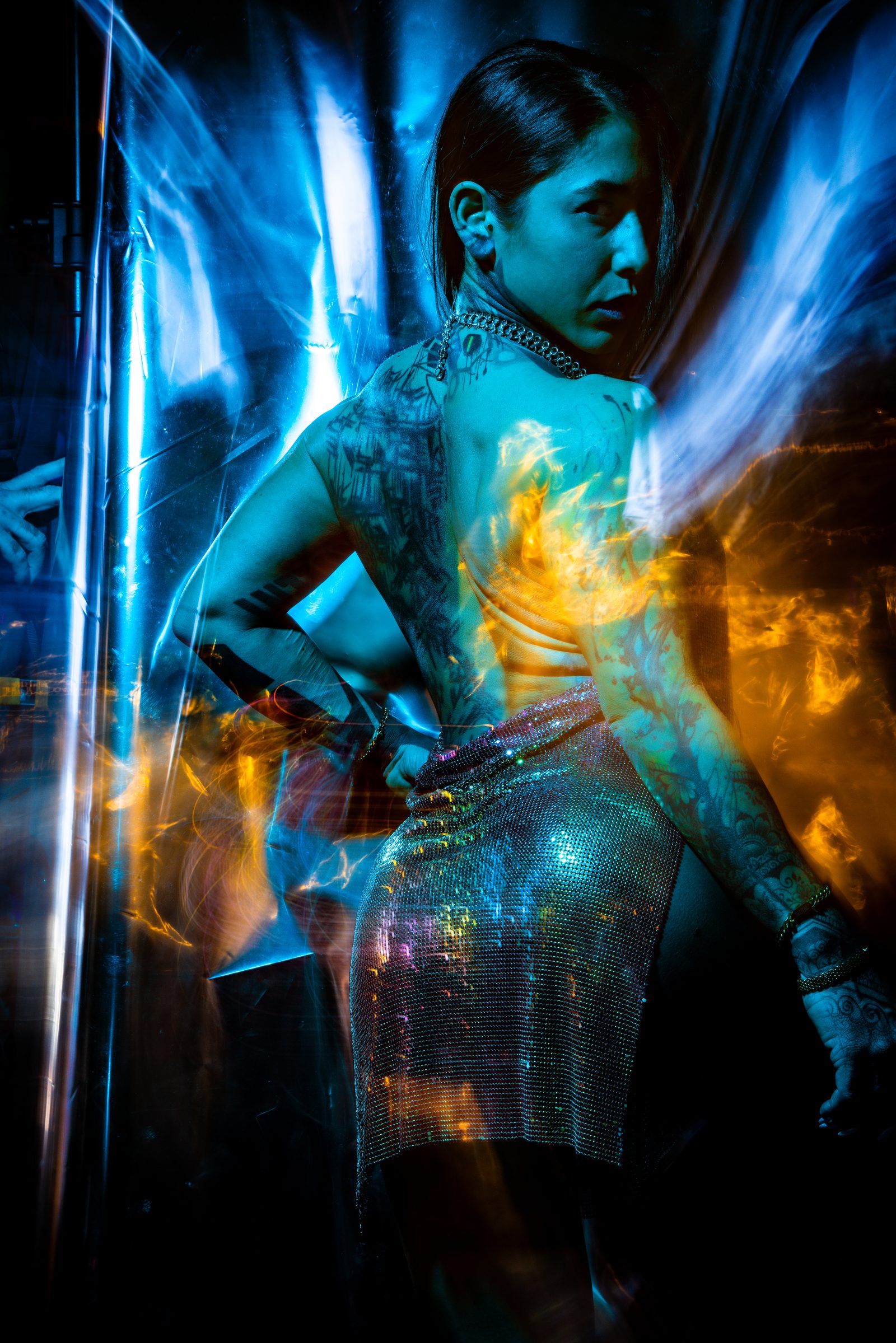Fire projected onto skin and a chainmail garment, seen through scratched glass in blue and amber, from the Light & Body series.