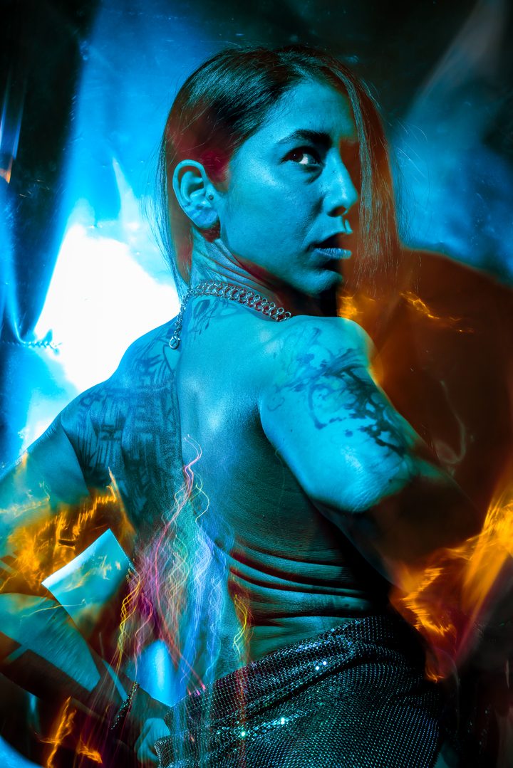 A figure surrounded by reflective material in amber and teal light, the surfaces fracturing the gelled color across the frame.