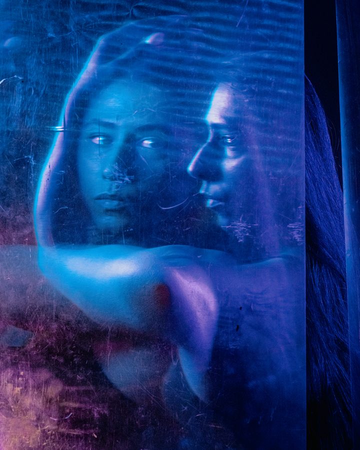 A portrait under a curtain of projected light points, the figure framed by rows of soft highlights in cool blue.