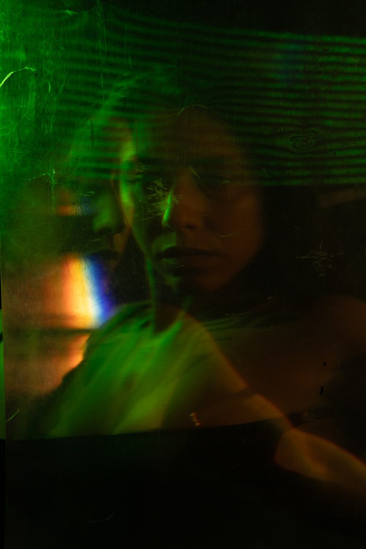 A figure caught in cool blue and violet light, the form doubled by motion against a soft field of projected highlights.